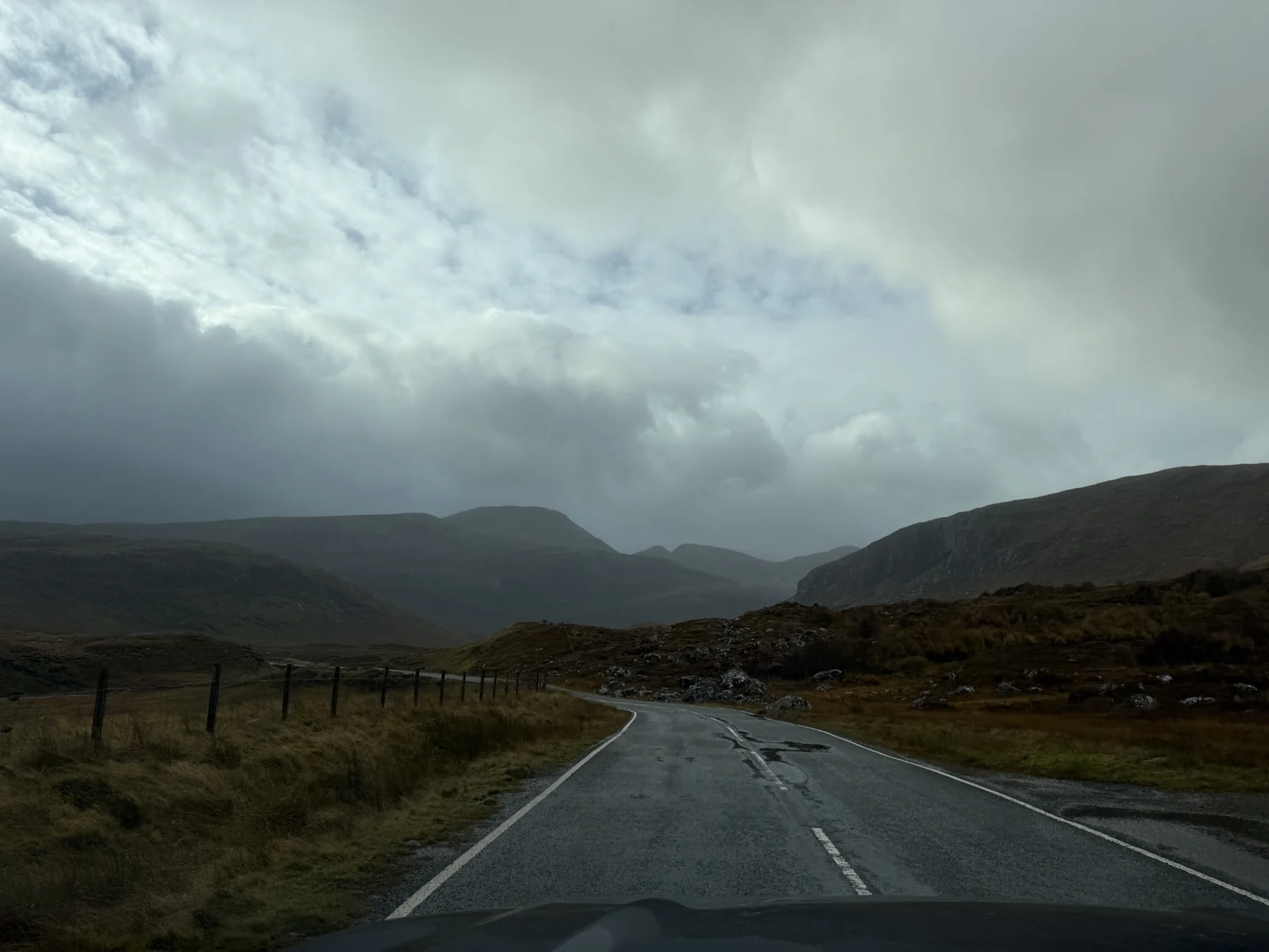 A wet road winding through remote hills beneath an overcast sky